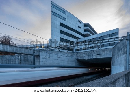 Ship like building with train tunnel and blurred train with inner lights visible coming out of a tunnel. Concrete constructions. Blue sky and clouds.