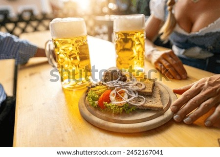 Traditional Bavarian Obatzda with pretzels and radishes and beer mugs, man and young woman in tracht in the background at beer garden or oktoberfest, Munich, Germany Royalty-Free Stock Photo #2452167041