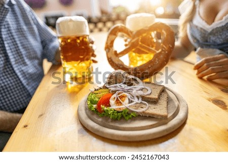 Bavarian Obatzda with pretzels and radishes and beer mugs, man and young woman in tracht in the background at beer garden or oktoberfest, Munich, Germany Royalty-Free Stock Photo #2452167043