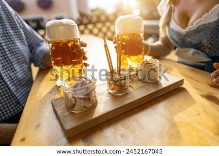 Bavarian Obatzda with pretzels and radishes and beer mugs, man and young woman in tracht in the background at beer garden or oktoberfest, Munich, Germany Royalty-Free Stock Photo #2452167045