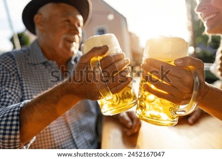 Senior man and woman in tracht toasting beer mugs in  traditional beer garden or oktoberfest at Bavaria, Germany, in summer Royalty-Free Stock Photo #2452167047