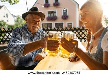 Senior man and woman in traditional clothing or tracht toasting beer mugs in beer garden or oktoberfest at Bavaria, Germany Royalty-Free Stock Photo #2452167055