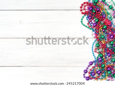 Colorful  Shiny Mardi Gras Beads on Rustic Painted White Board Background with room or space for copy, text, your words.  Horizontal with beads on side