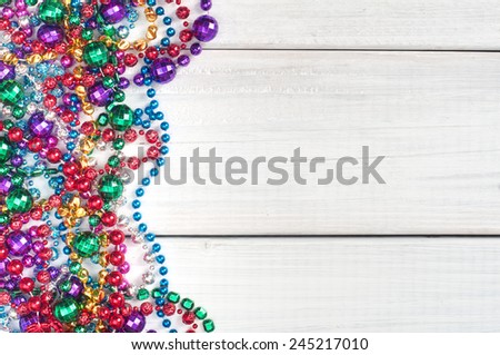 Colorful  Shiny Mardi Gras Beads on Rustic Painted White Board Background with room or space for copy, text, your words.   Horizontal with beads on side