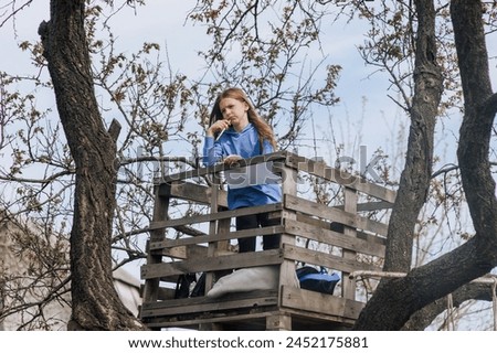 Beautiful pensive girl, inspired dreamy child teenager 8 years old stands on a wooden bridge outdoors in nature, writing poetry and drawing a picture of a landscape. Photography, portrait, lifestyle. Royalty-Free Stock Photo #2452175881
