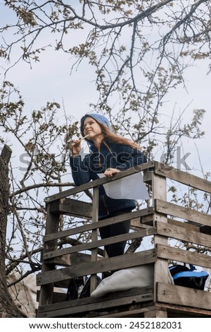 Beautiful pensive girl, inspired dreamy child teenager stands on a wooden bridge outdoors in nature, writing poetry and drawing a landscape picture. Photography, portrait.