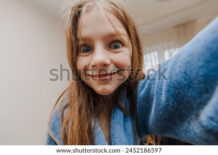 Smiling cheerful beautiful red-haired little girl, child teenager takes pictures of howling face holding camera, smartphone, phone in hands, laughing, grimacing. Photography, portrait, lifestyle.