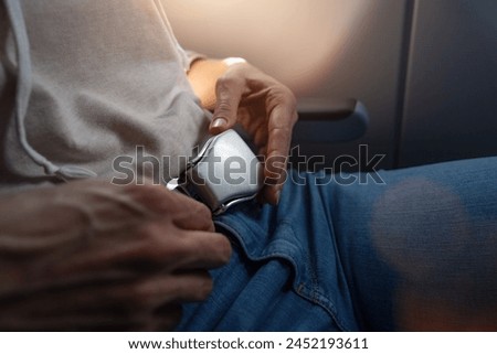 Close-up of a passenger securing a seat belt on an airplane, with a hand on buckle. safe flight on airplane concept image Royalty-Free Stock Photo #2452193611