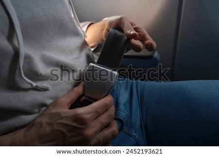 Close-up of a female passenger's hands fastening a seat belt on a plane. safe flight on airplane concept image