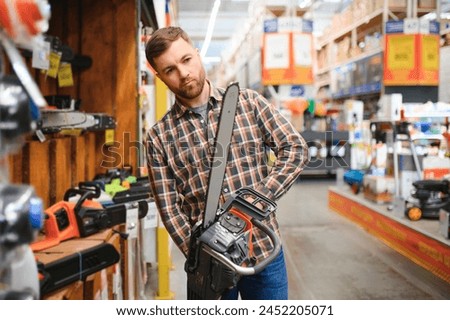 young male is standing with new electric saw in tools store.