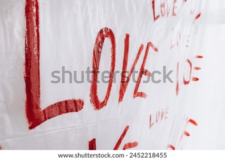 Multiple drawings of the word LOVE hand-painted in bright red forming a pattern on a plain white surface oilcloth, Valentine`s day concept celebration decoration in photo studio. Love, holiday, party