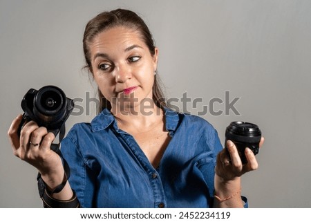 Young woman deciding between buying a new camera or a new lens. Woman with a camera and lens in her hands. Indecisive woman. Photography products Royalty-Free Stock Photo #2452234119