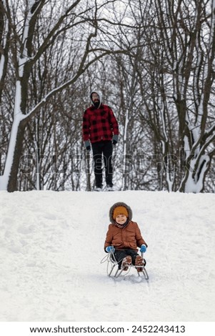 Portrait of happy little kid wearing winter knitted hat and blue mittens. Kid enjoying a sleigh ride on winter landscape. Child sledding riding a sleigh outdoors in snow. Vertical photo.