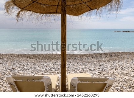 Photo of the beautiful beach in Altea, Alicante in Spain showing sun loungers and straw beach umbrellas on the pebble beach known as Playa La Roda