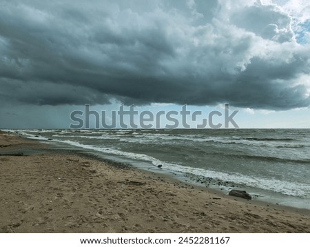 Wide sandy beach, rough sea, dark cloudy sky, brewing storm. Waves crashing, wind blowing sand. Ideal for illustrating stormy day at beach or as websiteapp background.