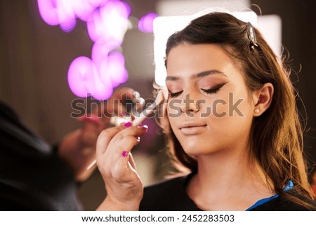 Professional beautician applying makeup on beautiful young woman's face. Professional make up studio work with gorgeous female model.