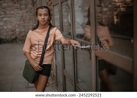 A beautiful girl with  handbag, dressed denim black shorts and a  T-shirt goes on the street of the city, posing against the background of brick walls and large windows