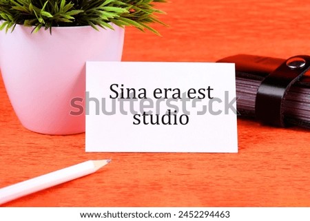 Sina era est studio It means Without anger and addiction it is written on a white business card next to a business card holder, pencil and plants in a white pot