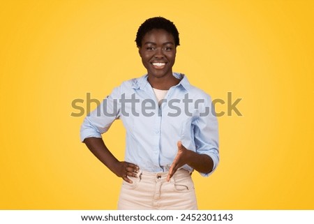A confident young african american woman smiling at the camera with her hands on her hips against a yellow background, exuding positivity and confidence Royalty-Free Stock Photo #2452301143