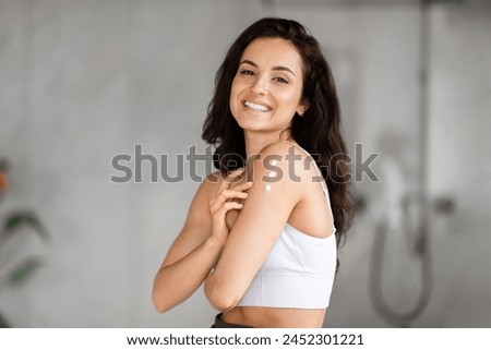 Happy young woman enjoys a skincare moment after morning shower, applying body lotion in her bathroom routine Royalty-Free Stock Photo #2452301221