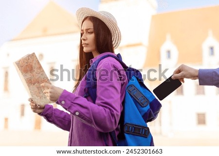 A millennial lady, appearing as a student, is absorbed in reading a map outdoors with European architecture in the background, unaware of being pickpocketed Royalty-Free Stock Photo #2452301663