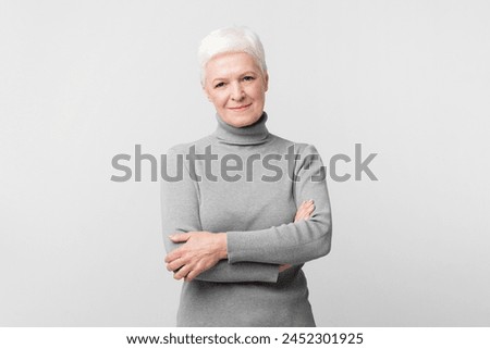 An elderly European woman stands confidently with a smile on grey background, perfect for s3niorlife promotion Royalty-Free Stock Photo #2452301925