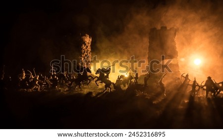 Medieval battle scene with cavalry and infantry. Silhouettes of figures as separate objects, fight between warriors on dark toned foggy background. Night scene. Selective focus Royalty-Free Stock Photo #2452316895