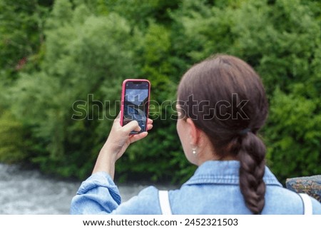A young woman is photographing the landscape with her smartphone. A girl takes pictures of nature on her smartphone. A girl with a smartphone in her. 