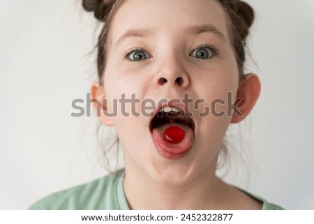 Funny little girl holding a pill on her tongue. A lollipop on the tongue of a little girl. Selected focus. High quality photo