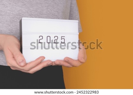 Hands hold lightbox with 2025 numbers in front of yellow background. New Year concept with plce for text.