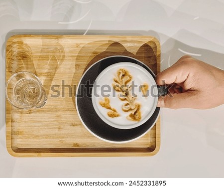 Top view of wooden tray with cup of capuccino latte coffee and glass of water with male hand, foam drink picture, breakfast mood