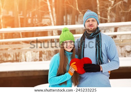 Young happy couple in love outdoors in the winter with a red heart in hands