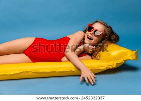 Happy child, red swimsuit, resting on inflatable mattress for swimming, hotel pool. Summer vacation, travel, resort. Little lady girl in bathing suit for beach blue background. Summer sea rest concept