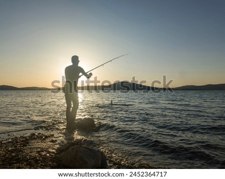 Fishing for pike, perch, carp. Fisherman with rod, spinning reel on sea or ocean. Man catching fish, pulling rod while fishing on sea, pond. Wild nature. The concept of rural getaway. Back view.  Royalty-Free Stock Photo #2452364717