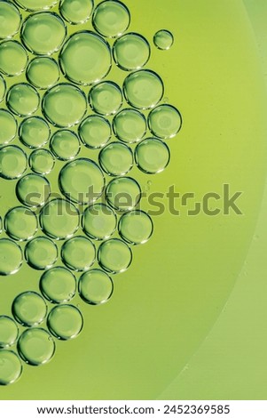 Abstract macro photograph of many water bubbles in oil on a green background.