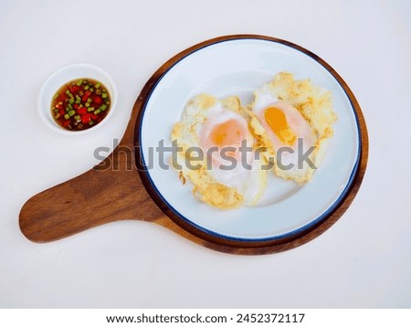 Fried chicken eggs were on a white plate on a wooden tray and there was fish sauce chili paste in a small bowl on a white background. It was a breakfast that I made myself.