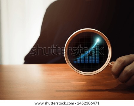 Business analytic chart, digital growth graph icon in round lens of gold magnifying glass in businessman's hand on dark background. Trends searching, money stock trading analysis, investment concepts.