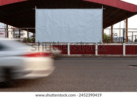 Blank white billboard on school wall Next to a road with cars passing in opposite directions.