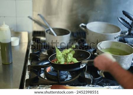 A man is cooking food on a stove with a bottle of oil next to him. Scene is focused and intense, as the man is carefully cooking his meal
