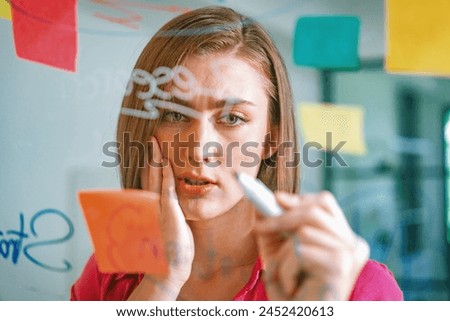 Closeup of young beautiful caucasian business leader presents marketing idea while writing marketing idea on glass board with mind map and colorful sticky notes. Portrait. Brainstorm. Immaculate. Royalty-Free Stock Photo #2452420613