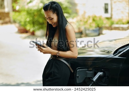 Smiling woman checking mobile app when waiting for car battery to fully charge Royalty-Free Stock Photo #2452425025