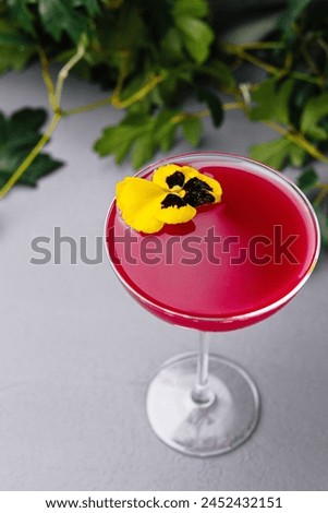 Vibrant pink drink in a coupe glass, adorned with a delicate edible pansy, symbolizing sophistication