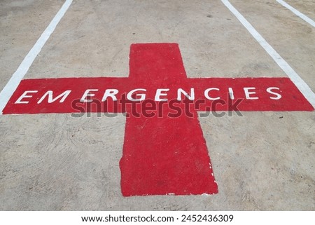 The letters EMERGENCIES on a red cross symbol. It was painted on the road as an emergency parking area.