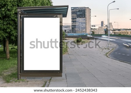 Blank White Bus Stop Vertical Poster Billboard Mockup In Front Of City Skyline Backdrop. Advertising Lightbox On The Sidewalk With Car Light Trails In The Background
