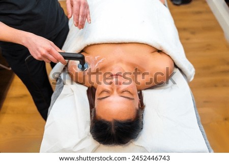 Massage therapist using the INDIBA machine to relieve shoulder pain of a patient lying on stretcher in a clinic Royalty-Free Stock Photo #2452446743
