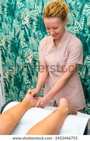 Vertical photo of a masseur giving a foot massage to a woman in the clinic