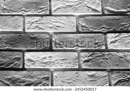 A black and white photograph of a brick wall with a rough texture and visible mortar joints. The bricks are laid in a traditional running bond pattern.