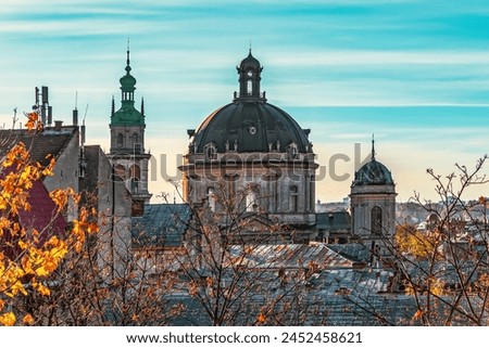 Dormition Church tower and Dominican Church dome in Lviv, Ukraine. Close-up of city roofs against the backdrop of bare tree branches on an autumn morning Royalty-Free Stock Photo #2452458621