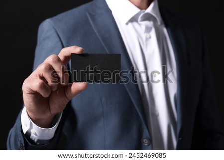 Businessman holding blank business card on black background, closeup