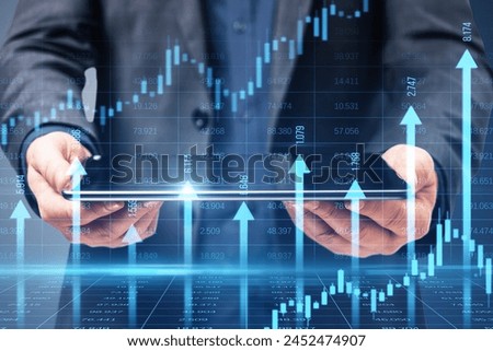 Close up of businessman hands holding tablet with growing blue vertical arrows and candlestick forex chart on blurry index grid background. Economic growth and increase concept. Double exposure